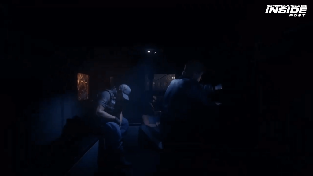 Scene from the trailer showing three characters in a van, with a dark lighting. One is facing away from the camera, another is looking down, and the third has their face hidden in shadows.